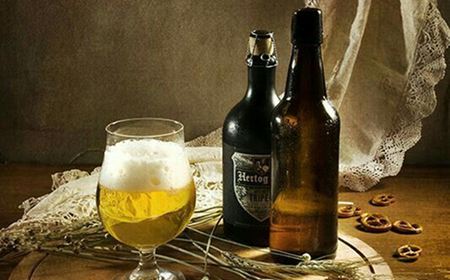 Бокал светлого пива с пеной и две тёмные бутылки пива на столе с кружевной тканью